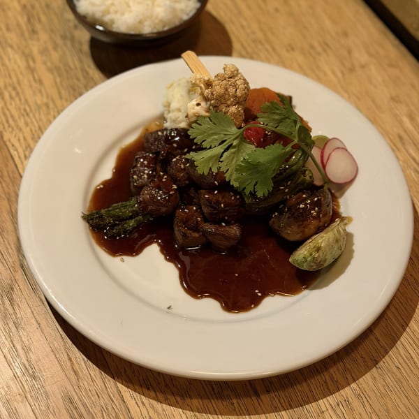 Teriyaki beef with asparagus, brussels sprouts, cauliflower, and cilantro on a white plate.