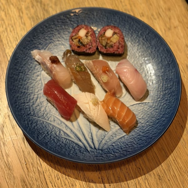 A blue patterned plate holds an assortment of nigiri and two sushi rolls on a wooden table.