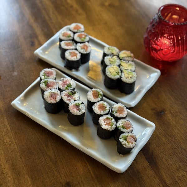 Two white rectangular plates filled with various sushi rolls on a wooden table with a red lantern.