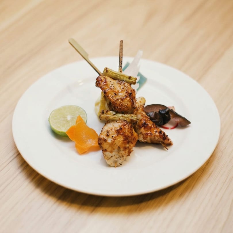 Grilled chicken skewers with lime, carrot, and mushrooms on a white plate.