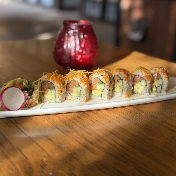 A plate of sushi rolls with salmon, avocado, and tobiko, garnished with radish and lemon zest.