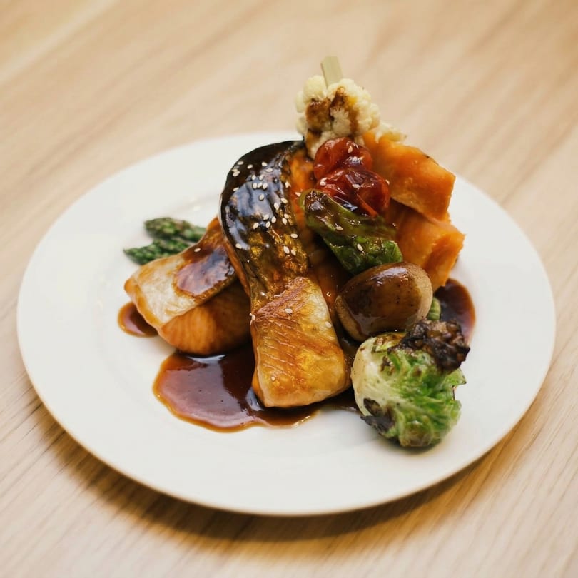 Glazed salmon with sesame seeds, roasted vegetables, and asparagus on a white plate.