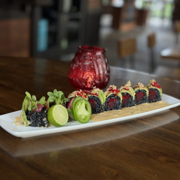 Black rice sushi rolls with tuna, avocado, red roe, lime, and jalapeño on a white plate.