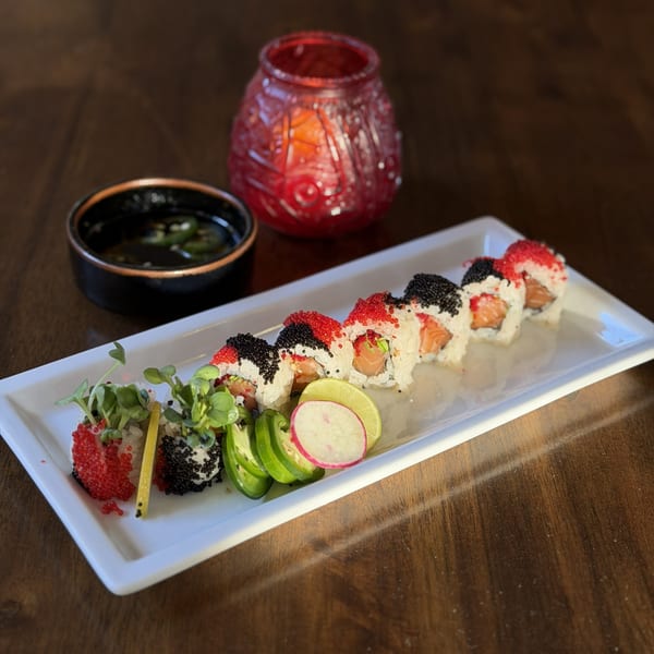 Sushi rolls with red and black roe, microgreens, and sliced vegetables on a white plate.