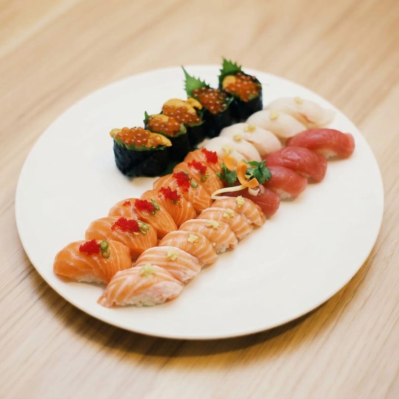 A white plate holds rows of various sushi, including salmon, tuna, and gunkan maki.