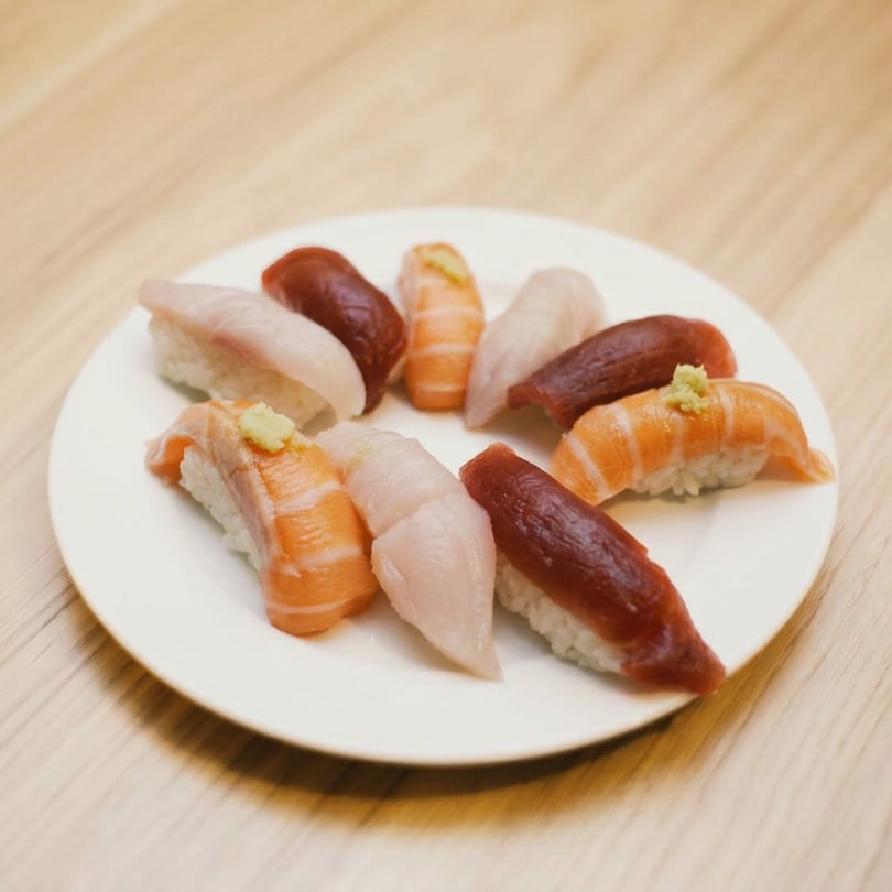 A white plate holds various pieces of nigiri sushi, including salmon, tuna, and white fish.