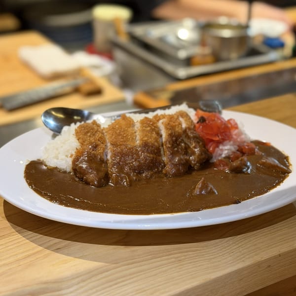 A plate of Japanese katsu curry with sliced fried pork cutlet, rice, and pickled ginger.